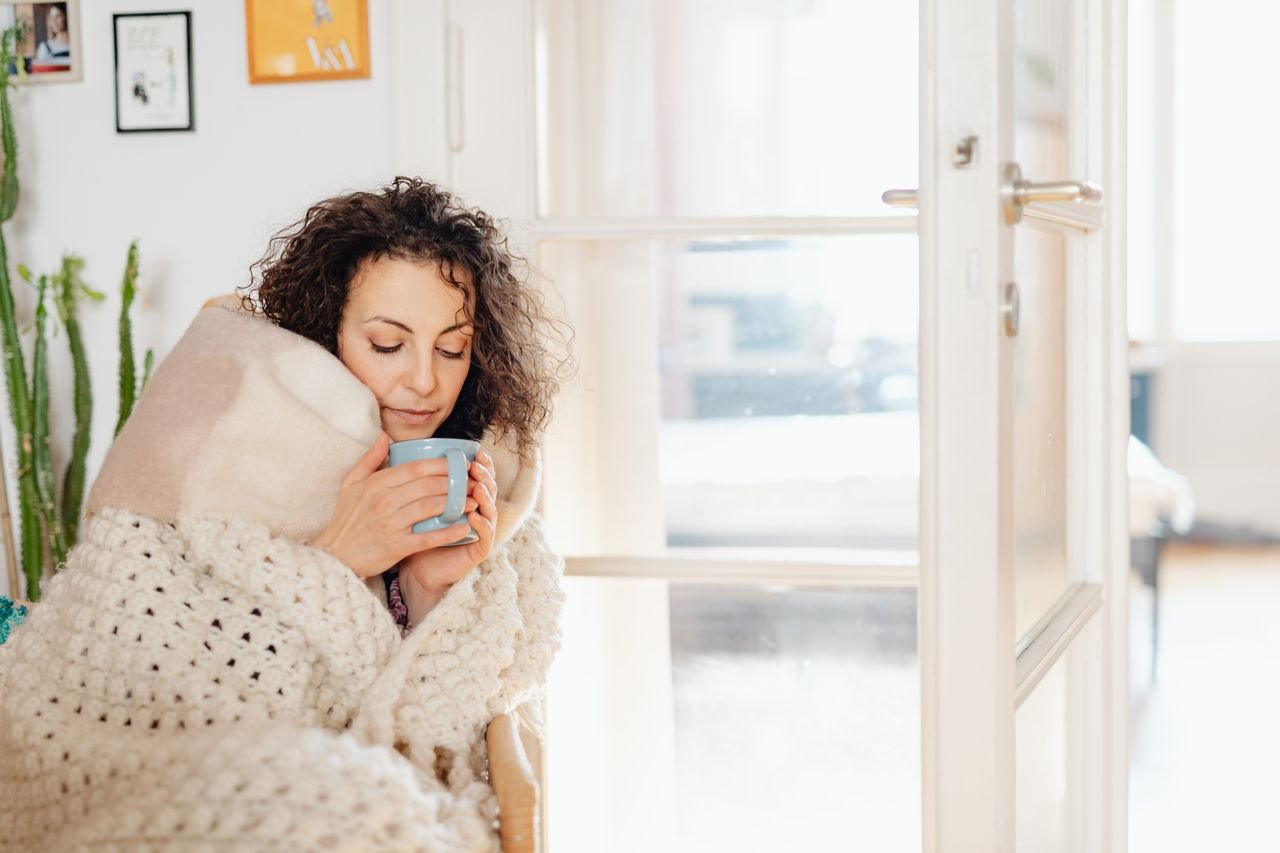 woman in cozy blanket holding a coffee mug on Sunday morning