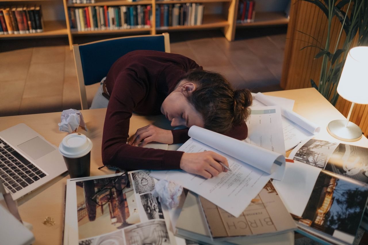 person lying on top of laptop and a lot of papers due to exhaustion