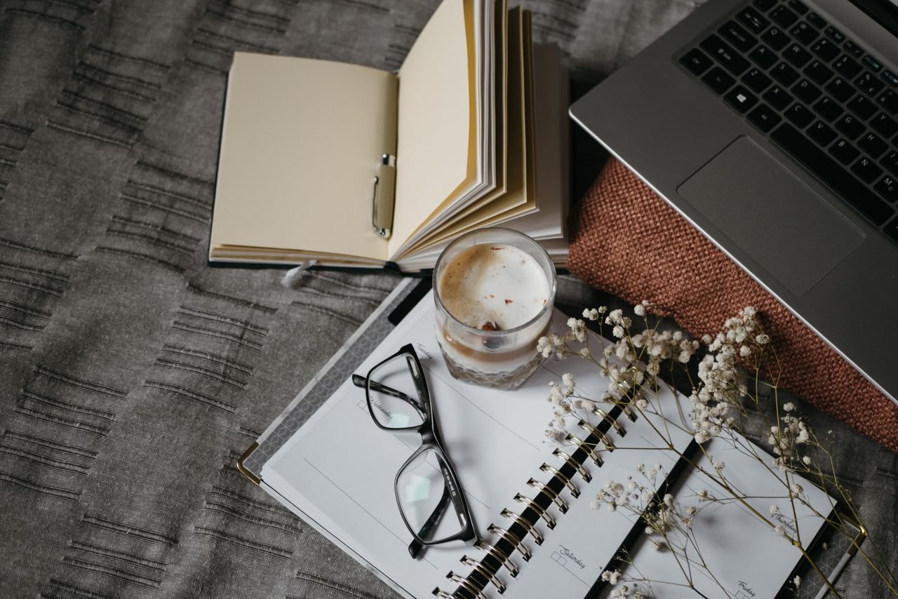 flat-lay of book, laptop and coffee in bed